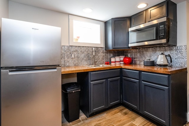 kitchen with butcher block countertops, a sink, appliances with stainless steel finishes, and backsplash