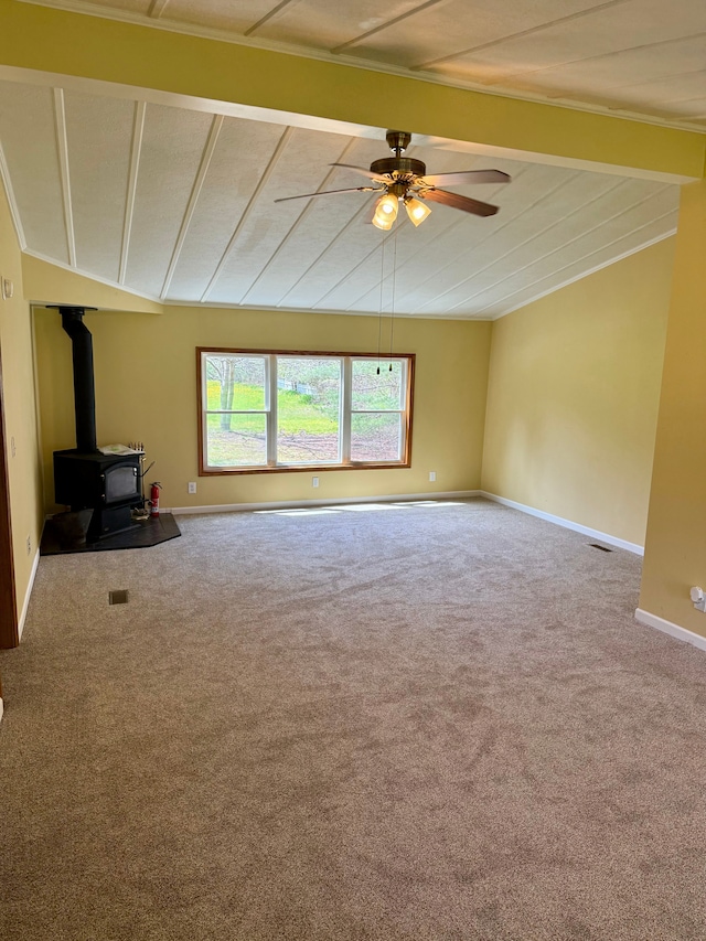unfurnished living room with carpet flooring, ceiling fan, a wood stove, baseboards, and vaulted ceiling