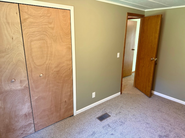 unfurnished bedroom featuring carpet flooring, crown molding, baseboards, visible vents, and a closet