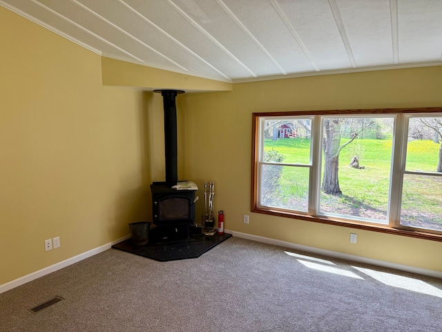 unfurnished living room featuring carpet floors, visible vents, ornamental molding, and a wood stove