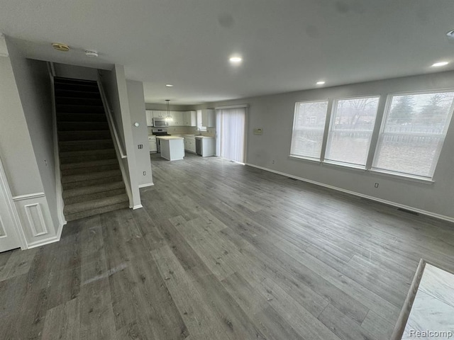 unfurnished living room with recessed lighting, baseboards, dark wood finished floors, and stairway