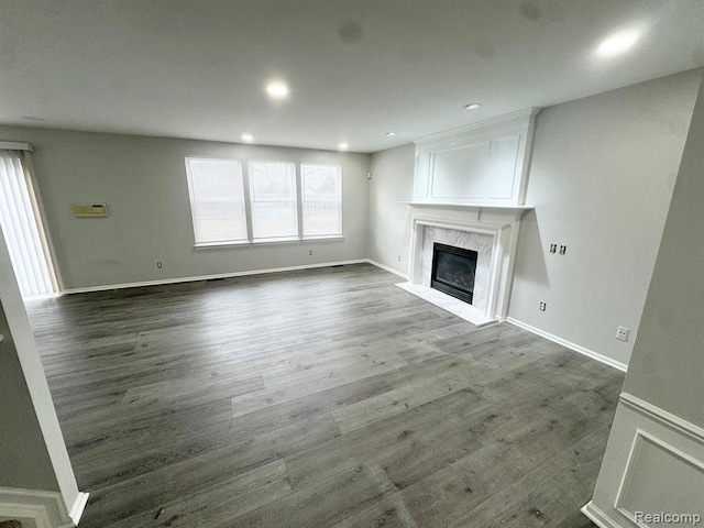 unfurnished living room featuring a high end fireplace, baseboards, recessed lighting, and wood finished floors