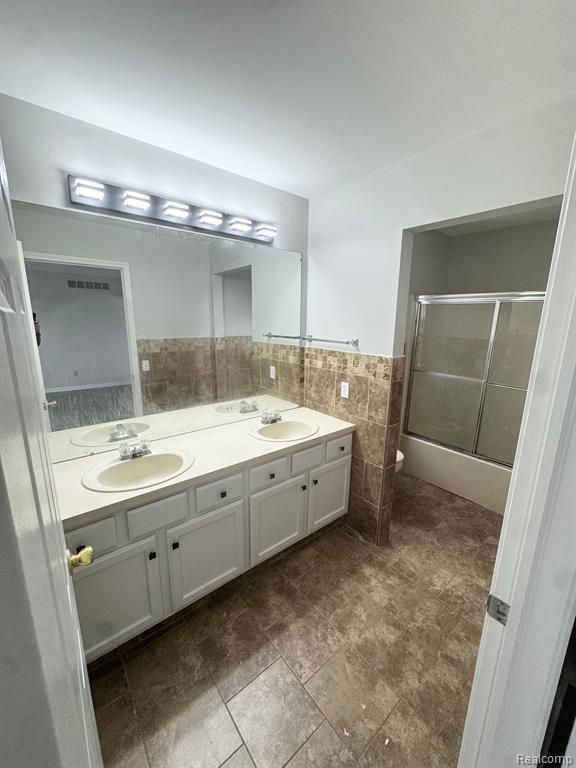 bathroom featuring a sink, tile walls, toilet, and double vanity