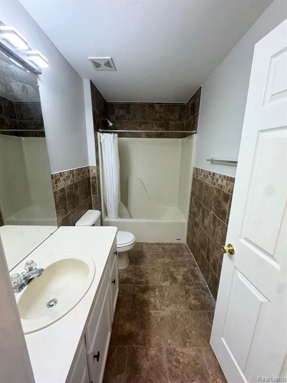 bathroom with visible vents, shower / tub combo with curtain, wainscoting, toilet, and tile walls
