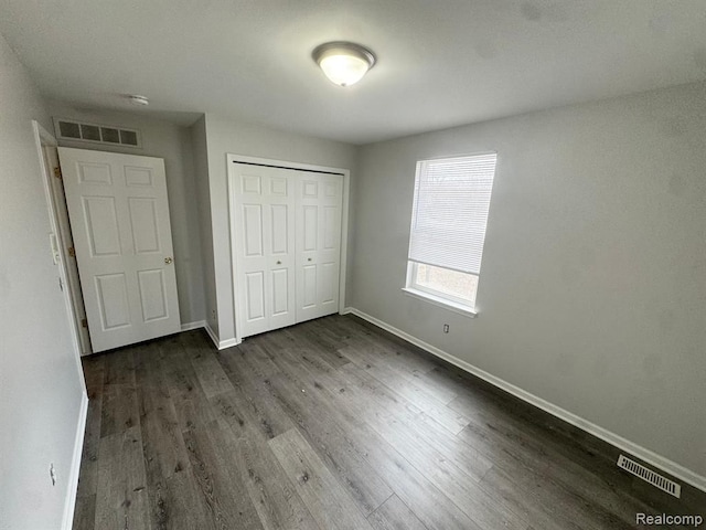 unfurnished bedroom with baseboards, a closet, dark wood-style floors, and visible vents