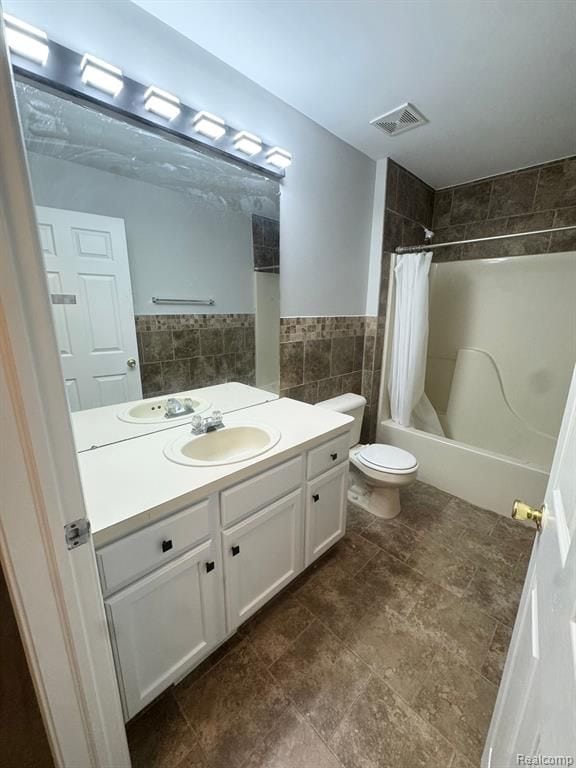 bathroom featuring vanity, toilet, shower / bath combination with curtain, tile walls, and visible vents