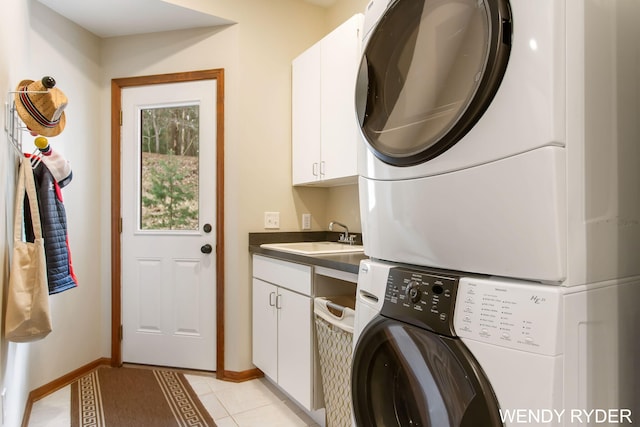 laundry room with cabinet space, stacked washing maching and dryer, baseboards, light tile patterned floors, and a sink