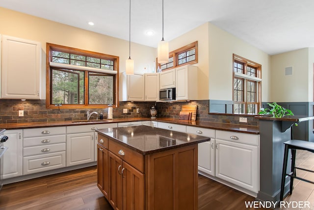 kitchen featuring tasteful backsplash, a sink, stainless steel microwave, dark wood-style floors, and white cabinetry