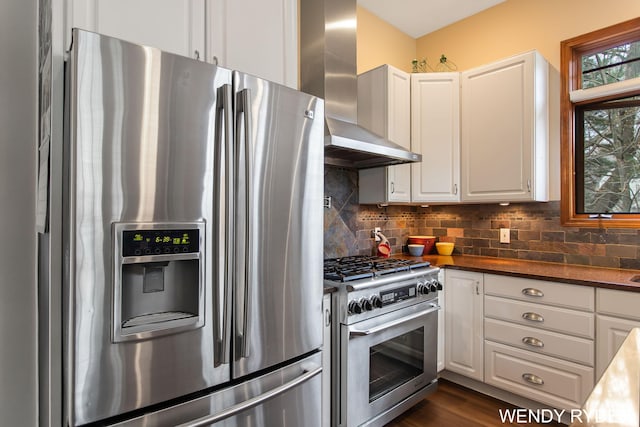 kitchen with wall chimney range hood, appliances with stainless steel finishes, tasteful backsplash, dark countertops, and white cabinetry