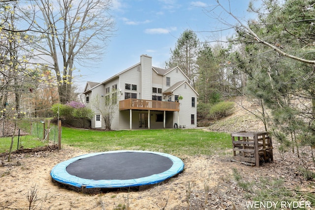 rear view of house featuring a trampoline, a chimney, a yard, and a deck