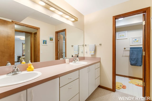 full bath with connected bathroom, double vanity, baseboards, and a sink