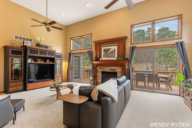 living area with visible vents, carpet floors, a towering ceiling, a fireplace, and a ceiling fan