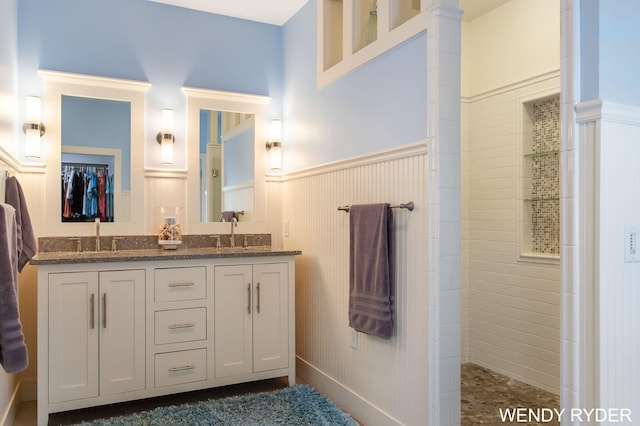 bathroom with double vanity, a sink, a walk in shower, and a wainscoted wall