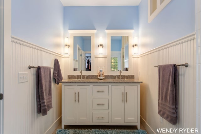 bathroom with a sink, a decorative wall, wainscoting, and double vanity