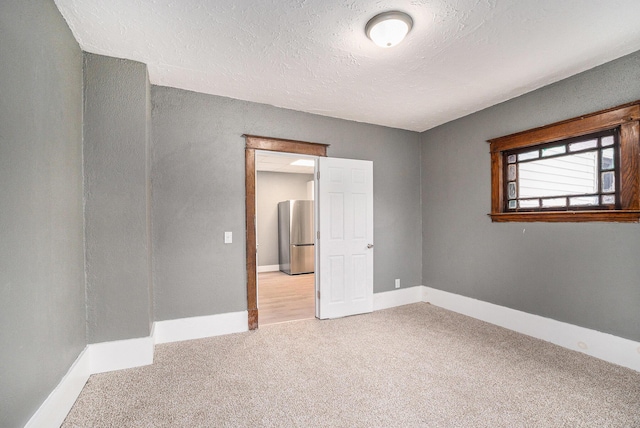 carpeted spare room with a textured ceiling and baseboards