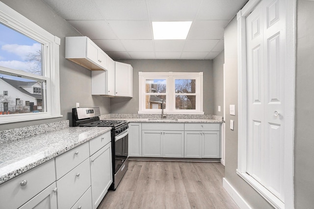 kitchen featuring gas range, light wood-type flooring, a sink, a drop ceiling, and white cabinetry