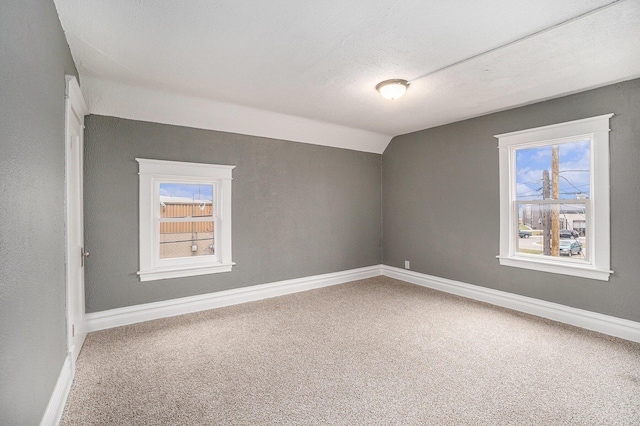 carpeted spare room with baseboards, plenty of natural light, and lofted ceiling