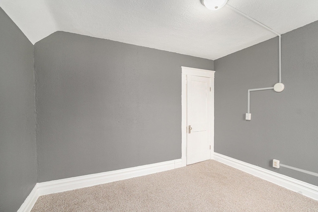 carpeted empty room featuring baseboards and vaulted ceiling