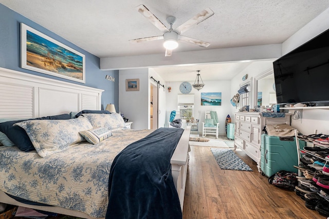 bedroom featuring a ceiling fan, a textured ceiling, a barn door, and wood finished floors