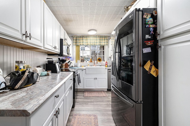 kitchen with wood finished floors, a sink, an ornate ceiling, stainless steel appliances, and white cabinetry