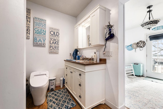 half bath with vanity, baseboards, toilet, and wood finished floors