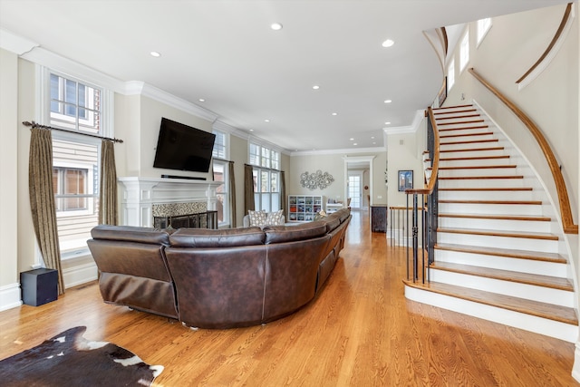 living room featuring crown molding, a fireplace, stairs, and light wood-style flooring