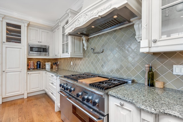 kitchen with glass insert cabinets, premium range hood, light stone counters, light wood-style floors, and stainless steel appliances