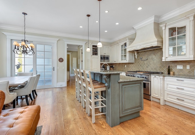 kitchen featuring appliances with stainless steel finishes, custom exhaust hood, ornamental molding, and a center island with sink
