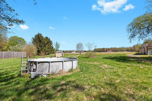 view of yard with a storage unit, an outdoor pool, fence, and an outbuilding