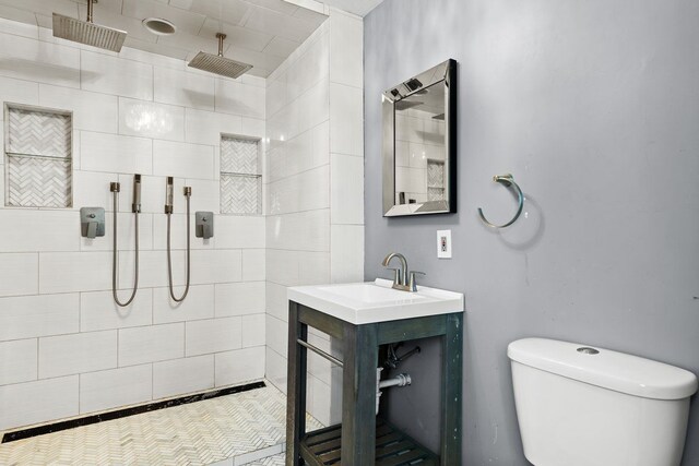 bathroom with toilet, tiled shower, and vanity