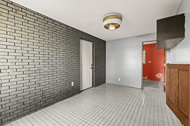 tiled empty room featuring brick wall