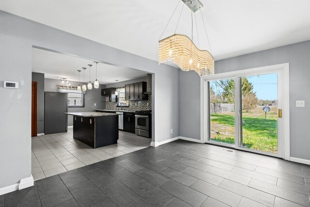 kitchen with a kitchen island, stainless steel range with electric stovetop, baseboards, freestanding refrigerator, and a notable chandelier
