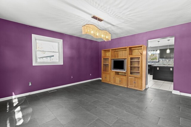 unfurnished living room with an inviting chandelier, baseboards, tile patterned flooring, and visible vents