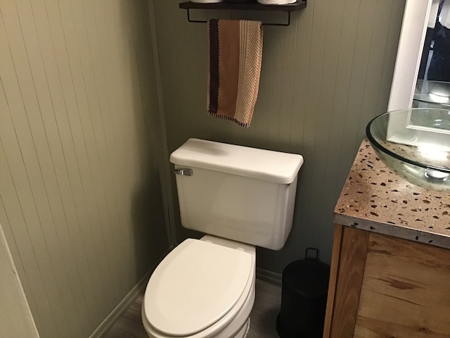 half bath featuring wooden walls, toilet, and vanity