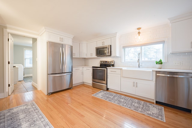 kitchen with backsplash, appliances with stainless steel finishes, a sink, and light wood-type flooring