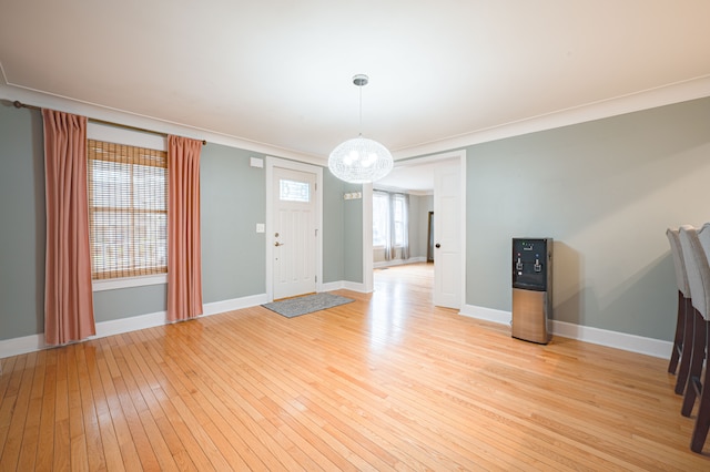 interior space with baseboards, a notable chandelier, ornamental molding, and light wood-style floors