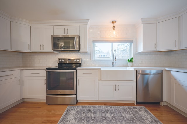 kitchen featuring decorative backsplash, appliances with stainless steel finishes, a sink, light wood finished floors, and white cabinetry