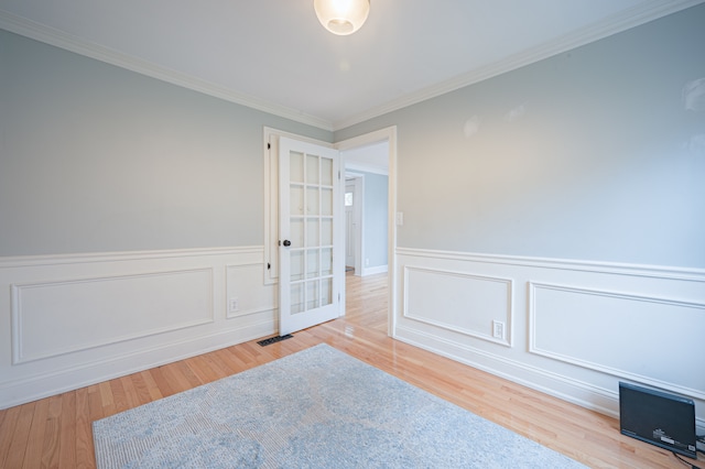 empty room with a wainscoted wall, ornamental molding, wood finished floors, and visible vents