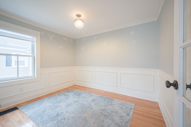 empty room with light wood-style flooring, wainscoting, and ornamental molding