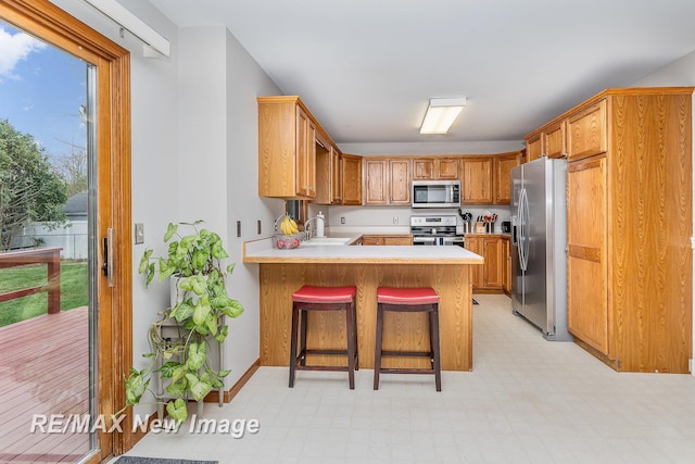 kitchen with a sink, appliances with stainless steel finishes, a peninsula, and light countertops
