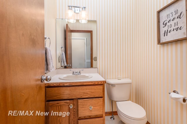 half bath with toilet, wallpapered walls, tile patterned floors, and vanity