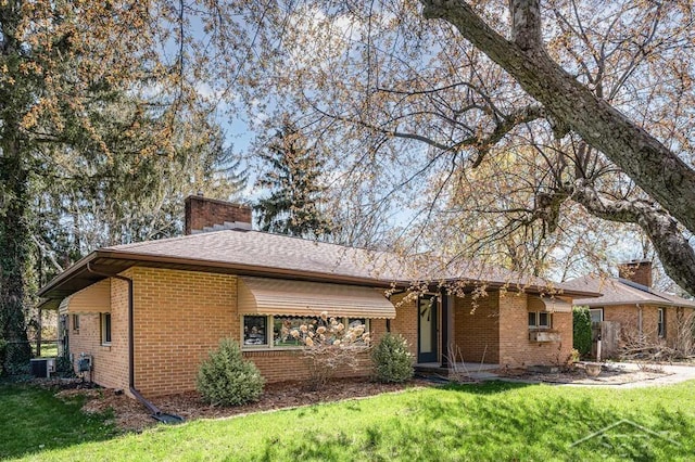 ranch-style home featuring brick siding, a chimney, central AC unit, and a front lawn