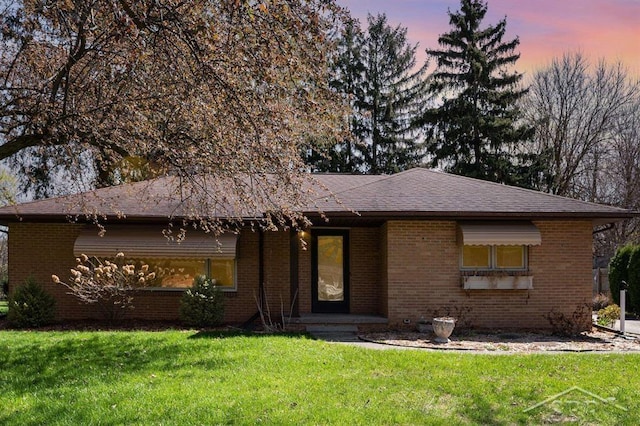 ranch-style house with brick siding, roof with shingles, and a yard