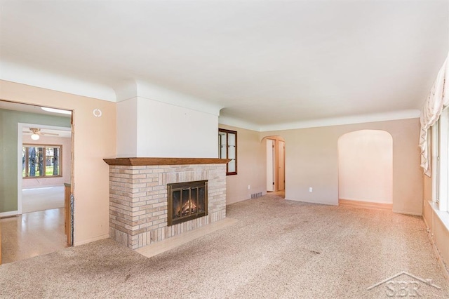 unfurnished living room with a ceiling fan, visible vents, arched walkways, a brick fireplace, and carpet