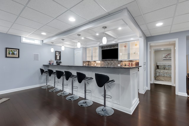 kitchen featuring dark wood-style flooring, a breakfast bar area, a peninsula, baseboards, and glass insert cabinets