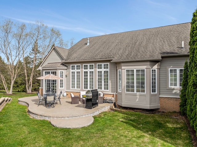 back of property featuring a lawn, a patio, a shingled roof, and brick siding