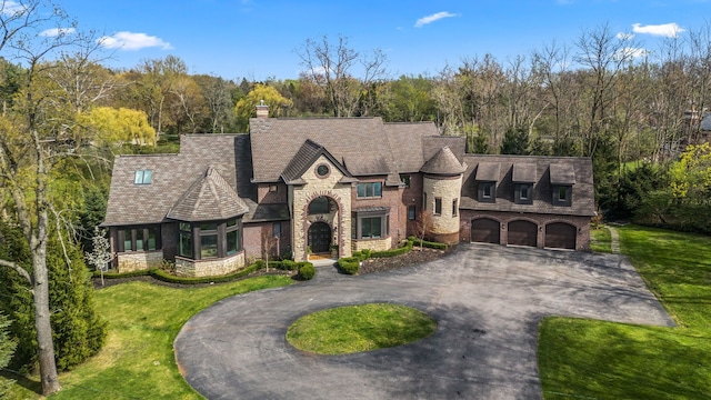 french country home with curved driveway, an attached garage, a front lawn, and stone siding