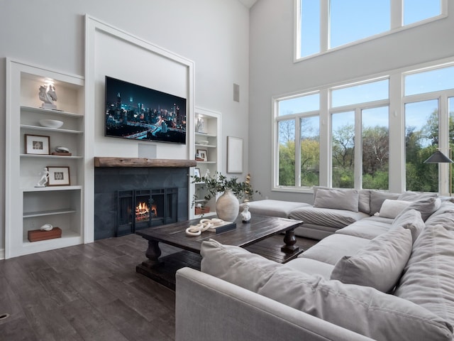 living area with a healthy amount of sunlight, built in features, a lit fireplace, and wood finished floors