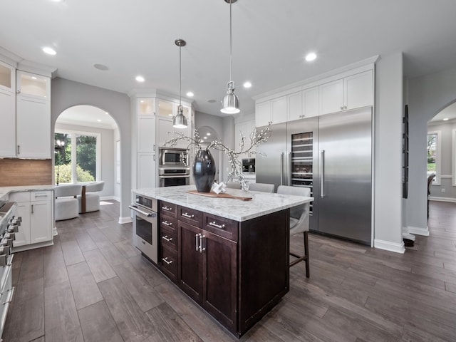 kitchen featuring built in appliances, arched walkways, white cabinets, and glass insert cabinets