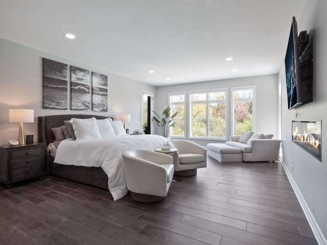 bedroom featuring dark wood-type flooring, recessed lighting, baseboards, and a glass covered fireplace